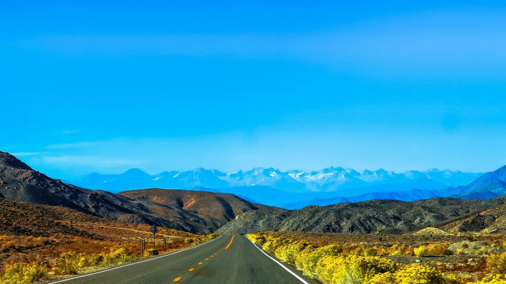 A straight road stretches towards snow-capped mountains in sunny Nye County, NV.